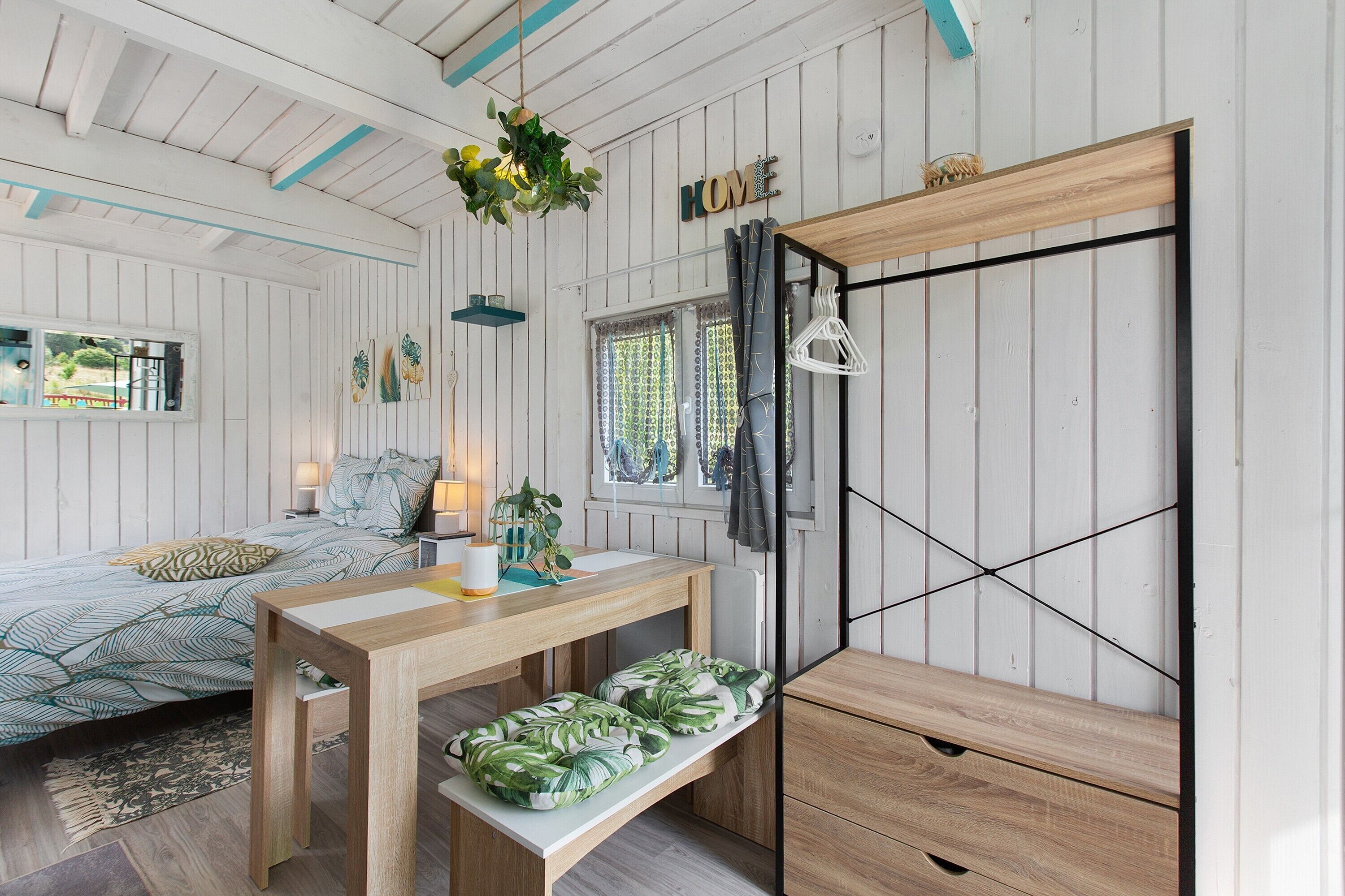 Une pièce comprenant un lit, une table en bois, un banc, un luminaire suspendu et une armoire.