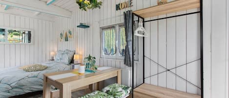 A room with a bed, a wooden table, a bench, a hanging light fixture, and a wardrobe.