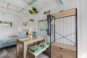 A room with a bed, a wooden table, a bench, a hanging light fixture, and a wardrobe.