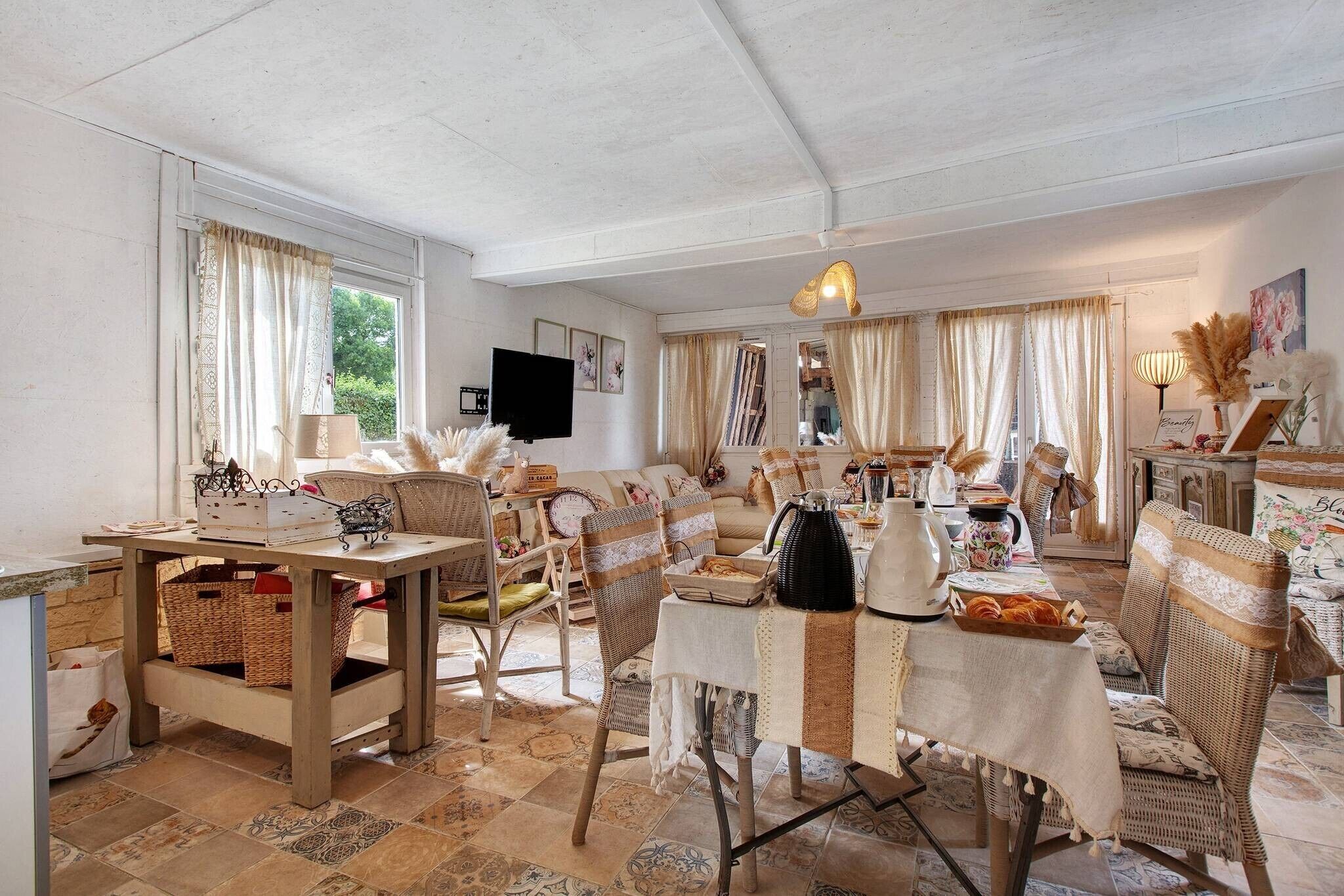A cozy living room with a dining area, wicker furniture, and a television on the wall.