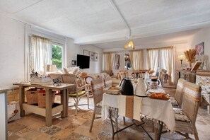 A cozy living room with a dining area, wicker furniture, and a television on the wall.