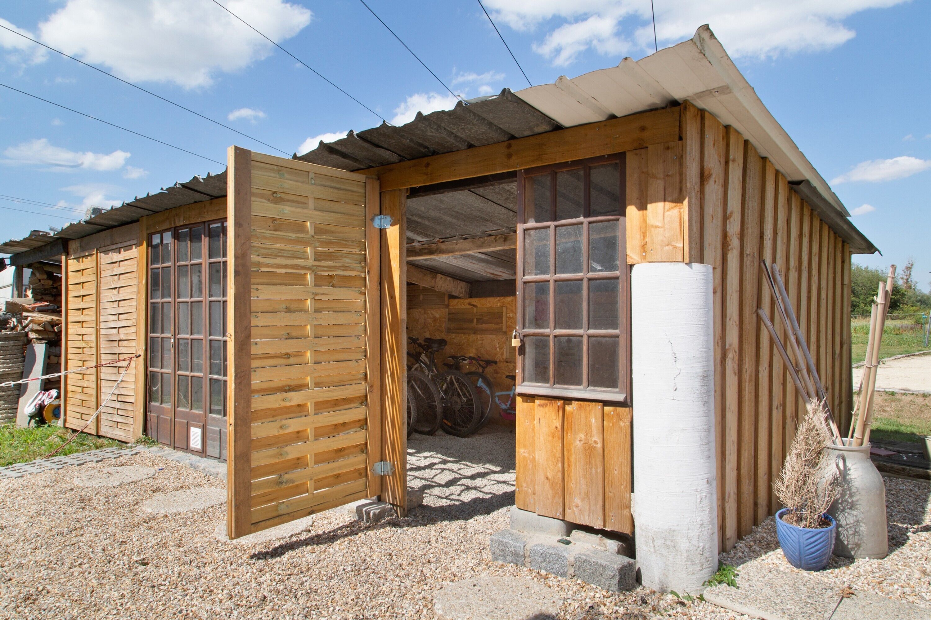 Une cabane en bois avec une grande porte ouverte, une fenêtre et un petit espace porche.