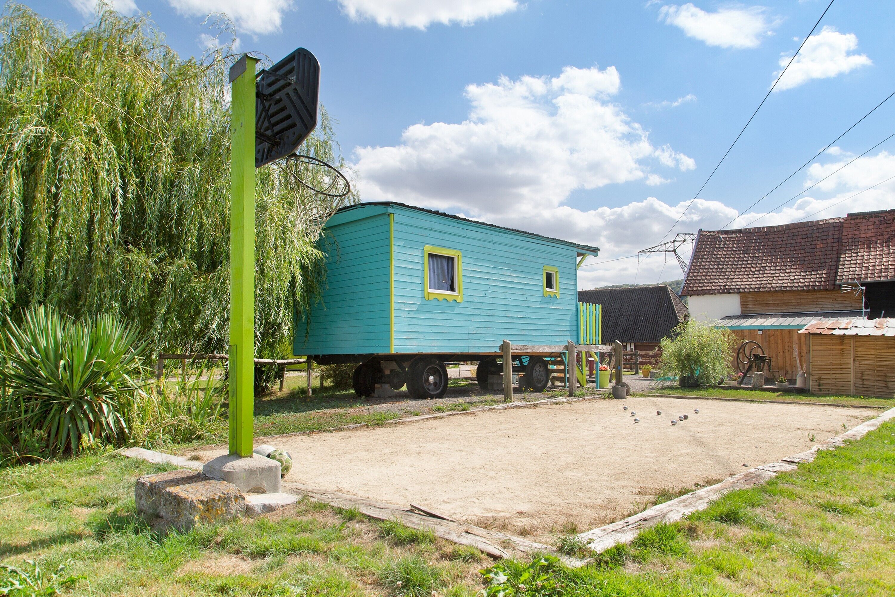 Une maison bleue avec un poteau vert et un petit abri de jardin, le tout situé dans un cadre rural.