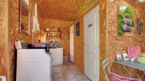 Eine kompakte Küche mit Kühlschrank, Spüle und einer kleinen Arbeitsfläche. Eine Tür führt in einen anderen Raum und ein Regal mit verschiedenen Gegenständen ist vorhanden.