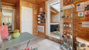 Ein Zimmer mit Holzboden, einer weißen Tür, einem Tisch mit einer Vase, einem Regal mit Büchern und einer Vitrine mit Flaschen.