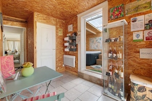 A room with a wooden ceiling, a white door, a table with a vase, a shelf with books, and a glass display case with bottles.