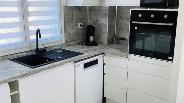 Eine moderne Küche mit weißen Schränken, einem eingebauten Geschirrspüler, einer Kaffeemaschine, einer Mikrowelle und einem Backofen.