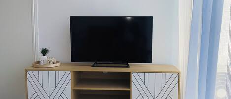 Una sala de estar con una televisión de pantalla plana sobre un mueble de madera, una mesita con un control remoto y un equipo de aire acondicionado en la pared.