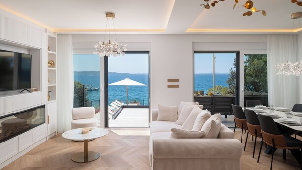 A modern living room with a large TV, a sofa, a dining area, and a view of the sea. - Villa Silvio (Kožino)