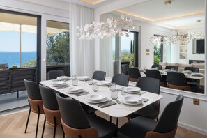 A dining area with a table set for six, large windows with a view of the sea, and a modern chandelier. - Villa Silvio (Kožino)