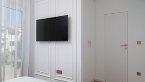 A room with a mounted television, a door with a golden handle, and a window with sheer curtains. - Villa Silvio (Kožino)