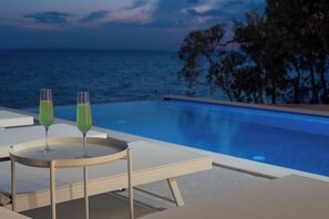 A poolside setting with two glasses of green beverage on a table, overlooking a pool and the sea. - Villa Silvio (Kožino)