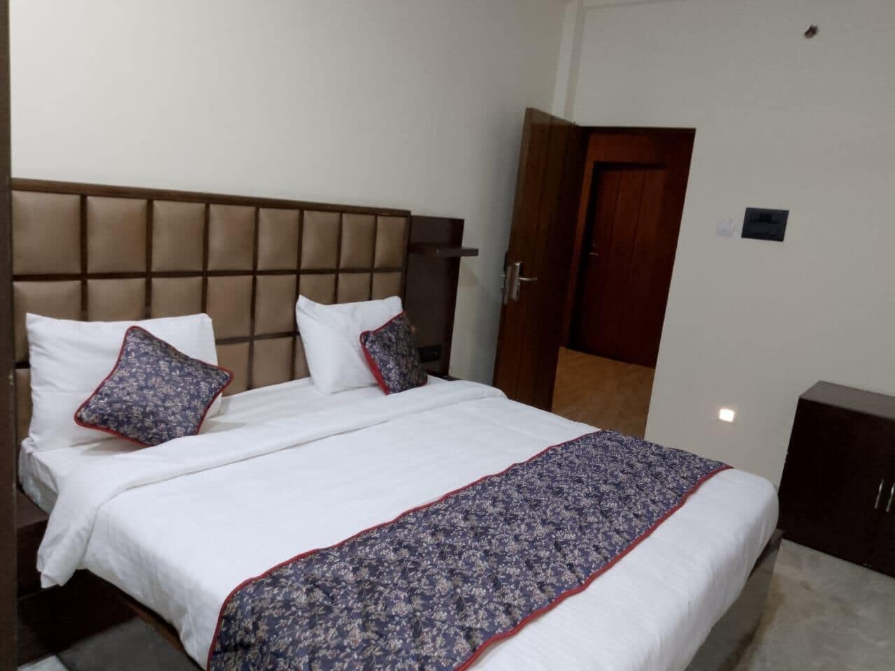 A neatly made bed with a patterned bedspread and pillows, a wooden headboard, and a closed door in the background.