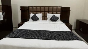 Una habitación de hotel con una cama grande, cabecera, mesita de noche, armario y ventilador de techo.