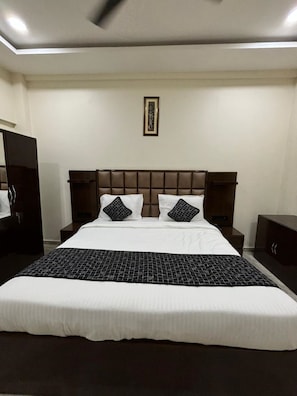 Una habitación de hotel con una cama grande, cabecera, mesita de noche, armario y ventilador de techo.