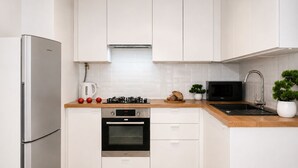 A modern kitchen with white cabinetry, a stainless steel refrigerator, an oven, a microwave, and a sink. - Lumina 2-room Apartment near Metro  (Warszawa)