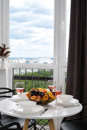 Ein Esstisch mit Obstschale und Weingläsern, vor einem Fenster mit Blick auf die Stadt.