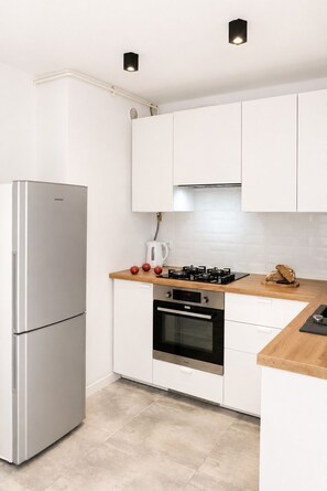 A modern kitchen with white cabinets, stainless steel appliances, and a wooden countertop. - Lumina 2-room Apartment near Metro  (Warszawa)