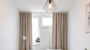 A neatly arranged bedroom with a wooden bed frame, a bedside table, a lamp, and a window with curtains. - Lumina 2-room Apartment near Metro  (Warszawa)