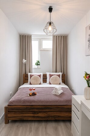 Ein ordentlich eingerichtetes Schlafzimmer mit einem Holzbettgestell, einem Nachttisch, einer Lampe und einem Fenster mit Vorhängen.