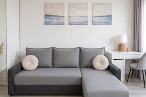A grey sectional sofa with two decorative pillows, a white desk with a lamp, and a chair. - Lumina 2-room Apartment near Metro  (Warszawa)