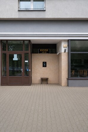 A building entrance with a kiosk labeled 'KIOSK' and a bench outside. - Lumina 2-room Apartment near Metro  (Warszawa)