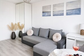 A modern living room with a grey sofa, a white side table, and a wine glass. - Lumina 2-room Apartment near Metro  (Warszawa)