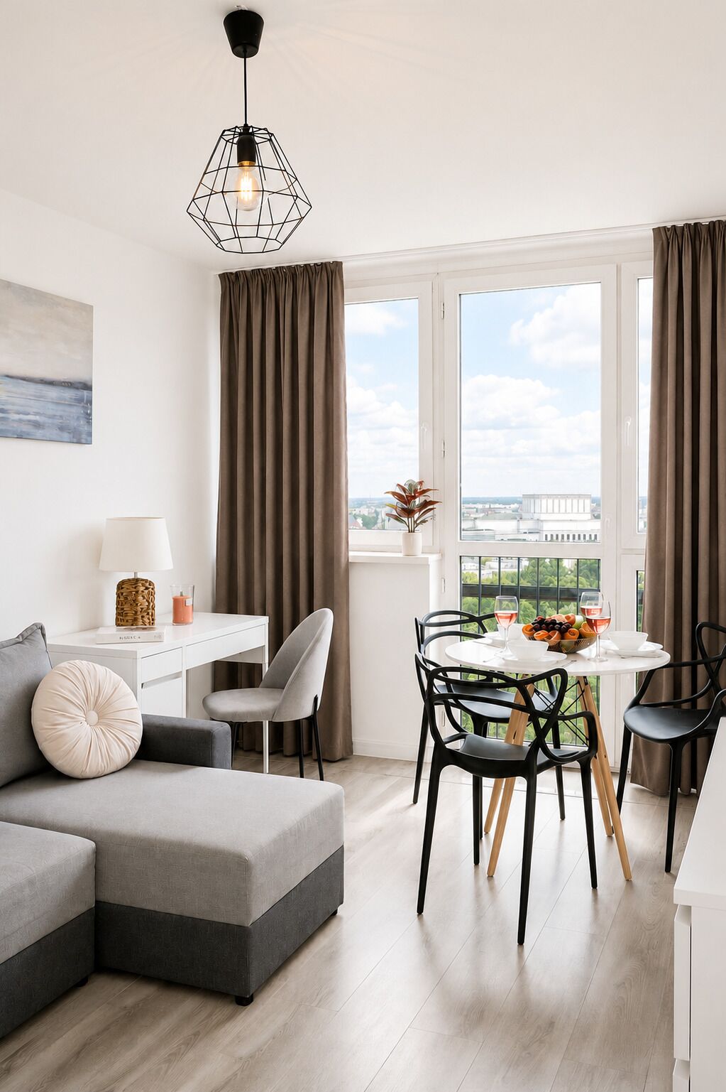 A modern living room with a grey sectional sofa, a dining table with chairs, a white desk, and a pendant light.