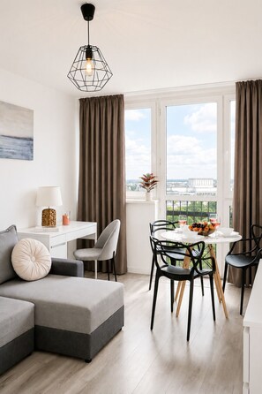 Een moderne woonkamer met een grijze modulaire bank, een eettafel met stoelen, een wit bureau en een hanglamp.