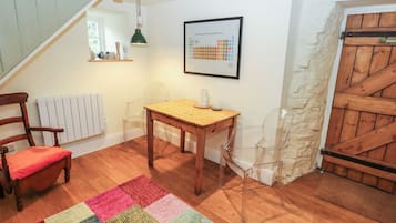 Une pièce avec une table en bois, une chaise, un tapis coloré, un tableau encadré représentant le tableau périodique du dialecte de Sheffield, et un escalier.