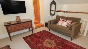 A living room with a flat-screen TV, a wooden console table with books, a brown sofa with pillows, a red patterned rug, and a wooden chair. - Laneside Barn (Hope Valley)