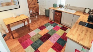 A compact kitchen with a wooden table, a sink, and a colorful rug. - Laneside Barn (Hope Valley)