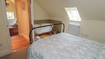 Une chambre à coucher avec un lit, une fenêtre, un puits de lumière, une salle de bain avec une baignoire et un radiateur.