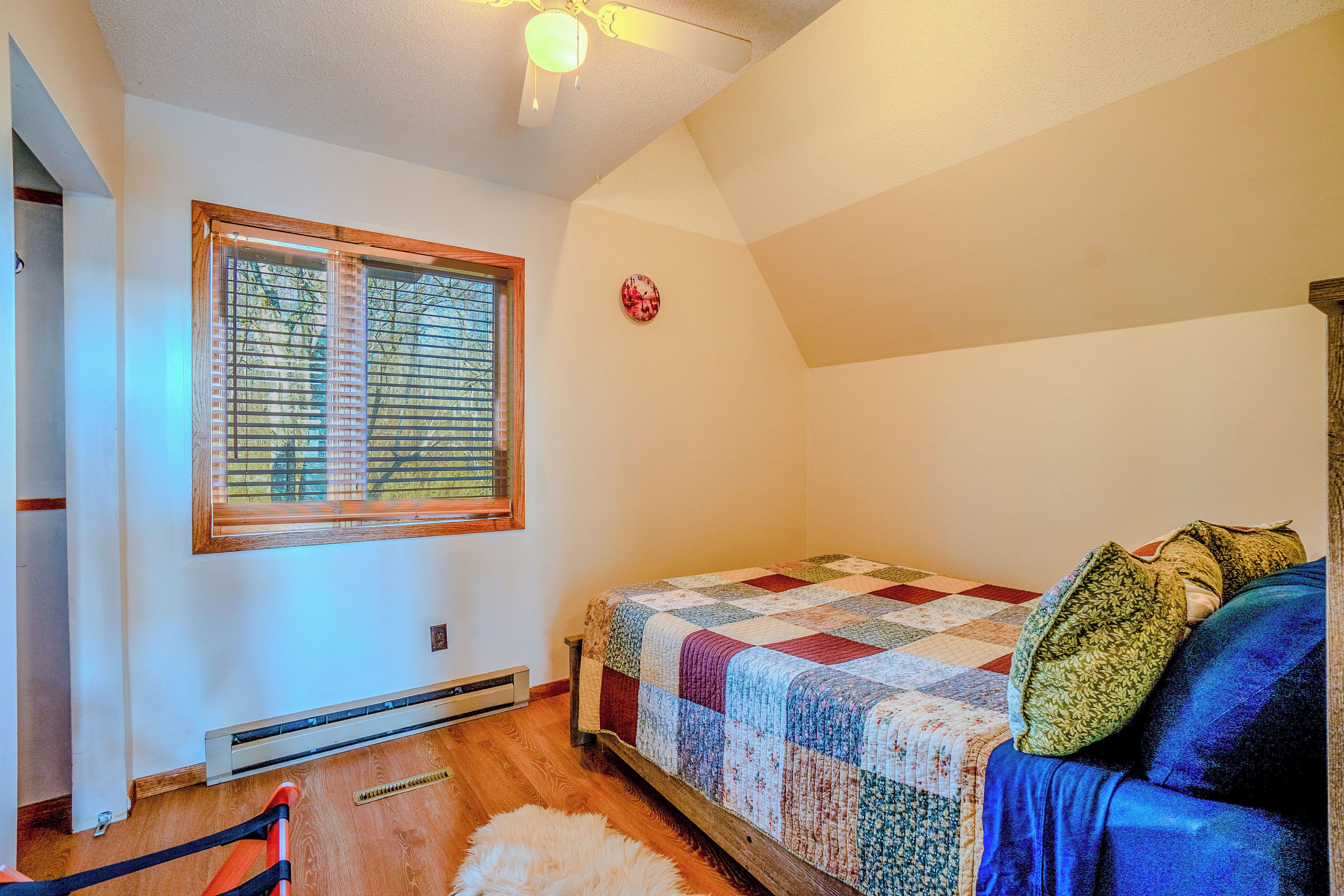 Ein Schlafzimmer mit Holzboden, einem Bett mit Quilzdecke, einem Fenster mit Jalousien, einer Wanduhr und einem Heizkörper.
