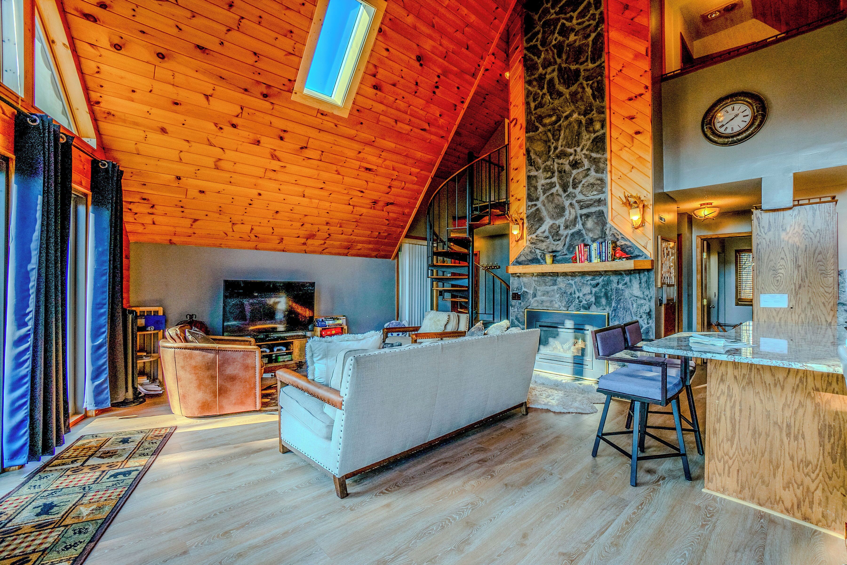 A spacious living room with a high ceiling, a stone fireplace, and a television.