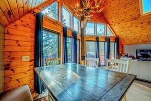 A wooden interior with a large dining table, multiple windows, and a chandelier.