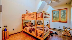 Un lit superposé avec une structure en bois, une fenêtre avec des stores et un ventilateur de plafond.