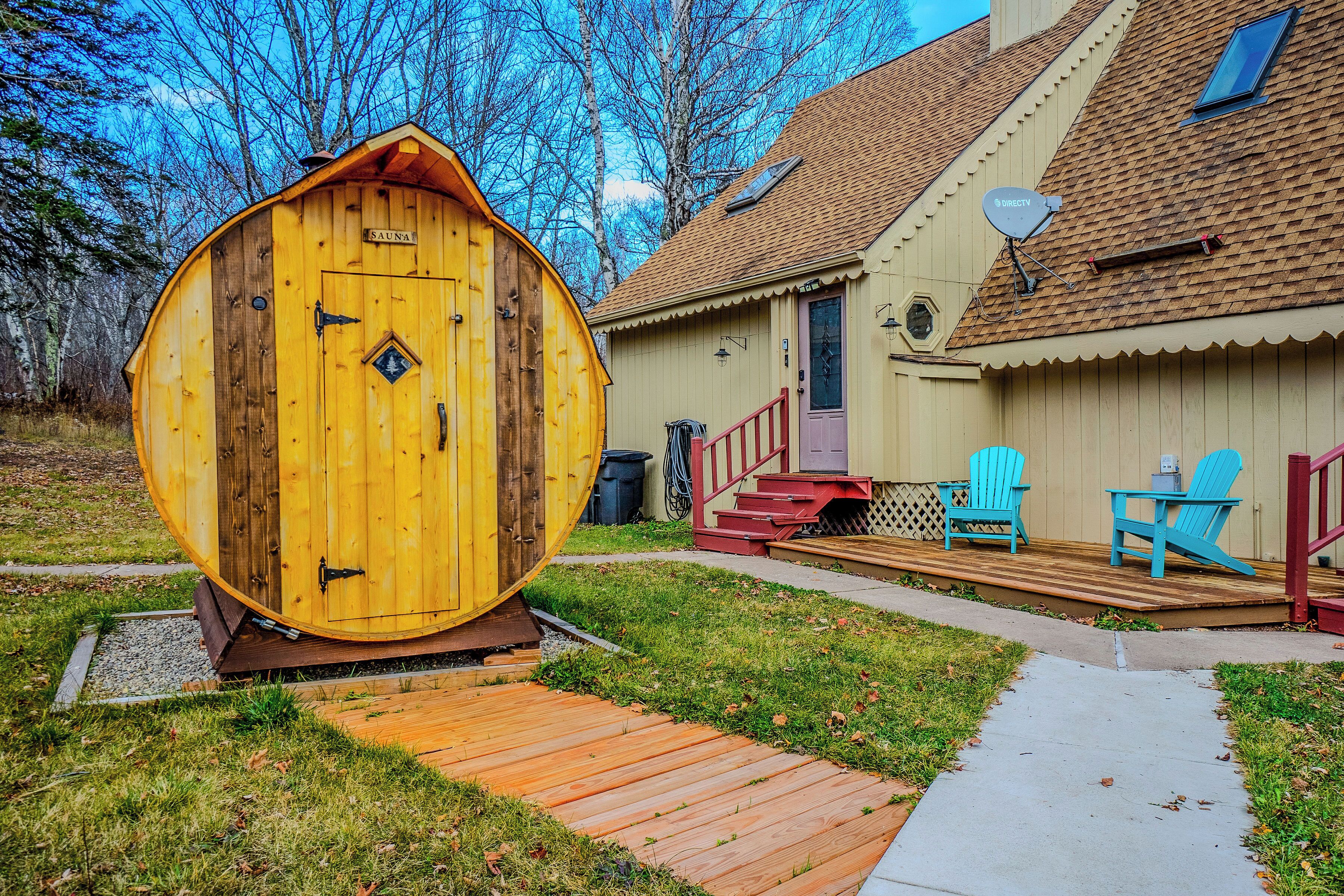 Eine Holzsauer mit Tür, eine Terrasse mit Stühlen und ein Haus mit Satellitenschüssel.