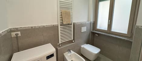 Un baño con lavadora, bidé y ventana de vidrio esmerilado.