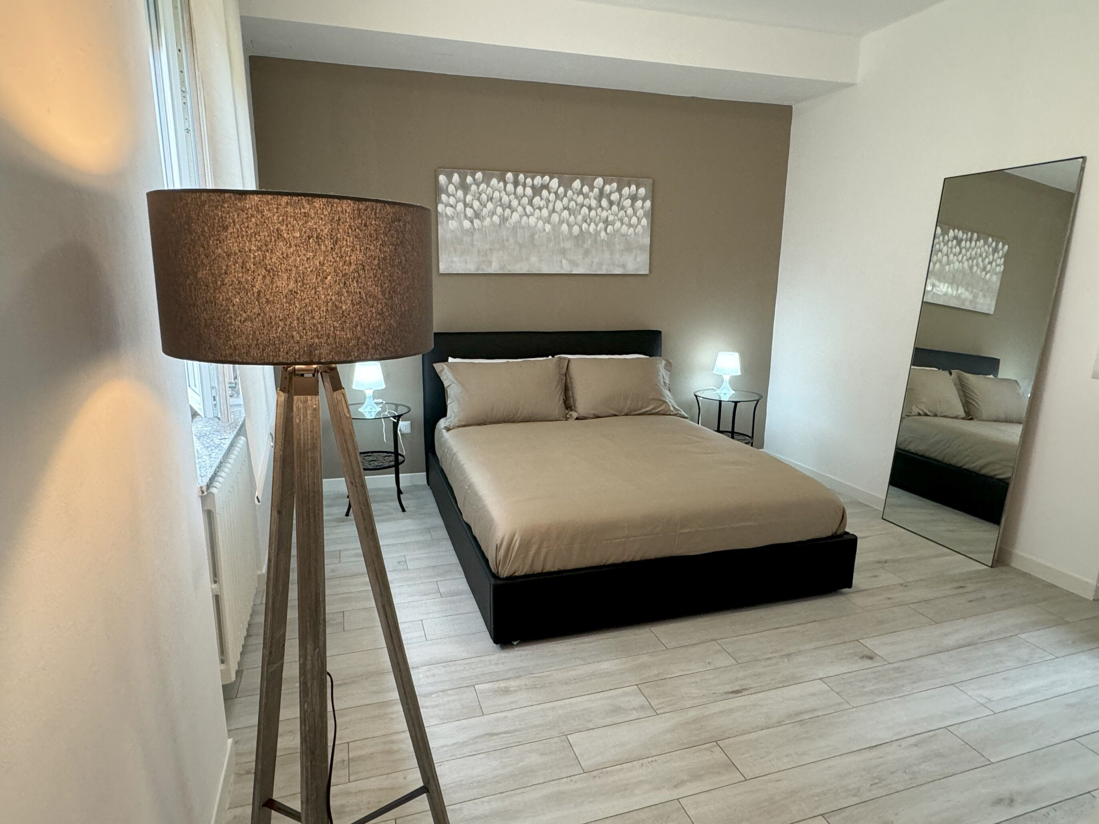 Un dormitorio con cama, lámpara de pie, una obra de arte en la pared y espejo.