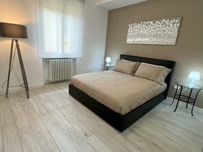 Ein modernes Schlafzimmer mit einem Bett, Nachttischen, einer Stehlampe und einer Heizung.