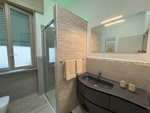 Ein modernes Badezimmer mit Duschkabine aus Glas, einem Waschtisch mit schwarzem Becken und einem Spiegel darüber.