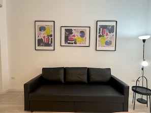Ein schwarzes Sofa mit drei gerahmten abstrakten Kunstwerken an der darüberliegenden Wand.
