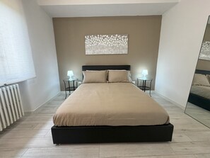 A modern bedroom with a large bed, two bedside tables with lamps, a radiator, and a wall-mounted artwork. - Am'Arena Apartment - Sleeps 4, 300 meters from the Arena (Verona)
