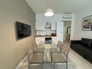 Ett modernt kök med vita skåp, en inbyggd ugn och en matplats med ett glasbord och stolar.