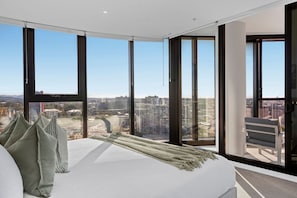 A modern bedroom with a large bed, multiple windows, and a city view. - Rooftop Infinity Pool! 5 Guests - Free Park & Gym (Fortitude Valley)