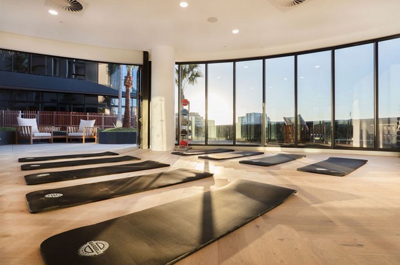 A yoga studio with mats arranged on a wooden floor, large windows, and a view of the city.