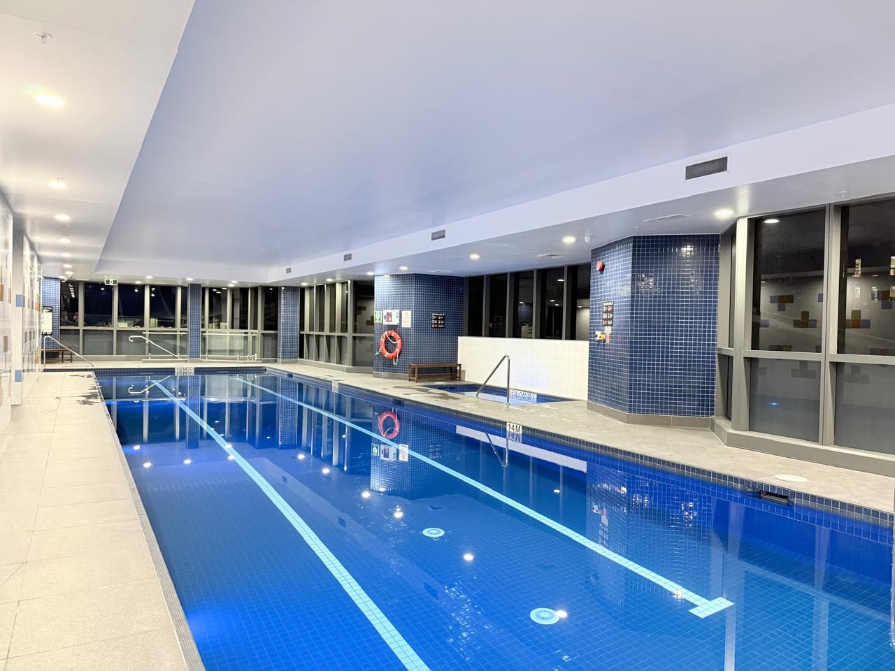 An indoor swimming pool with clear lane markings, a lifebuoy, and a tiled wall with a blue pattern.