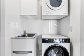 A compact laundry room with a front-loading washing machine and a stainless steel sink. - River Views from Level 43 | Free Parking, Pool & Gym (Brisbane City)