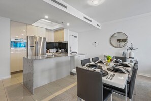A modern kitchen with stainless steel appliances, a dining area with a white table set for four, and a large mirror on the wall. - City Skyline from Level 37 | Free Parking, Pool & Gym (Brisbane City)